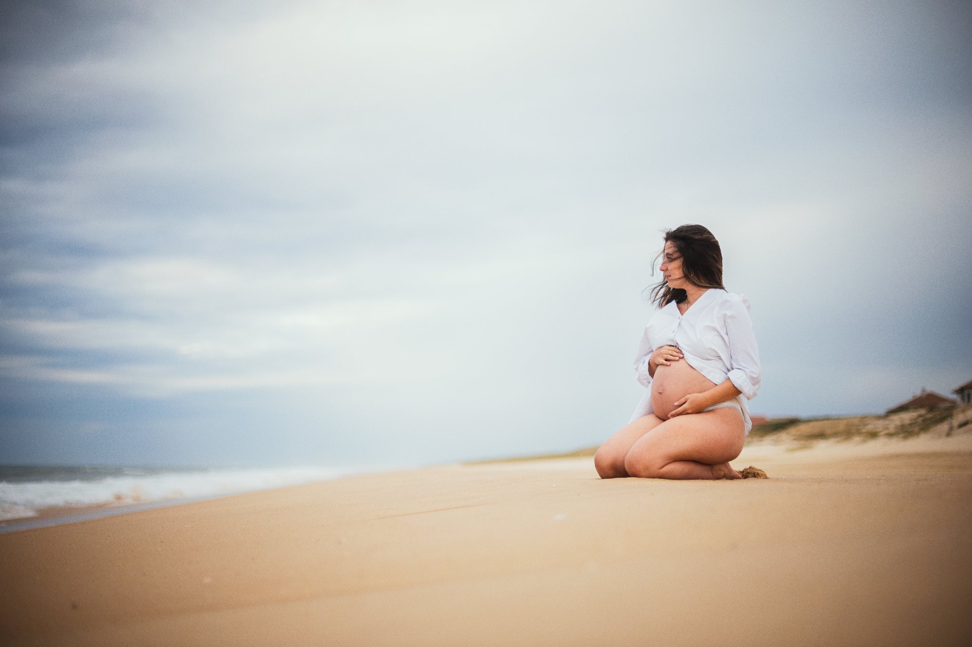 Séance photo grossesse sur la plage, future maman assise face à l'océan